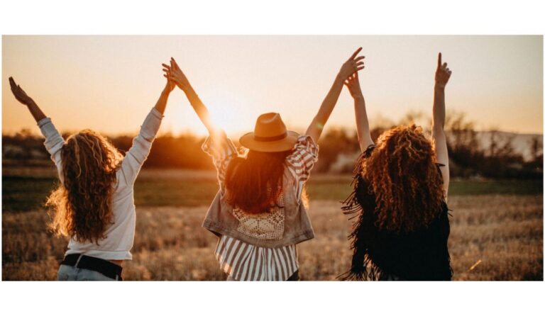 3 jeunes filles de dos qui lèvent les bras devant un coucher de soleil